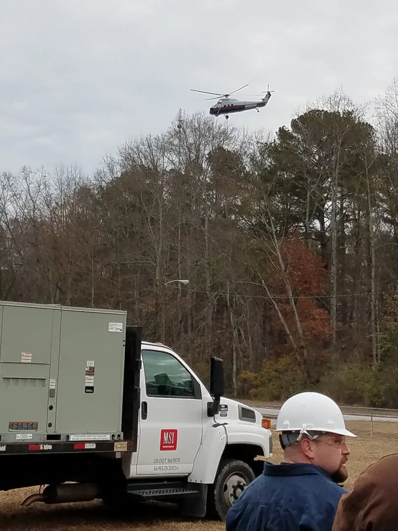 A man in hard hat next to a truck and helicopter.