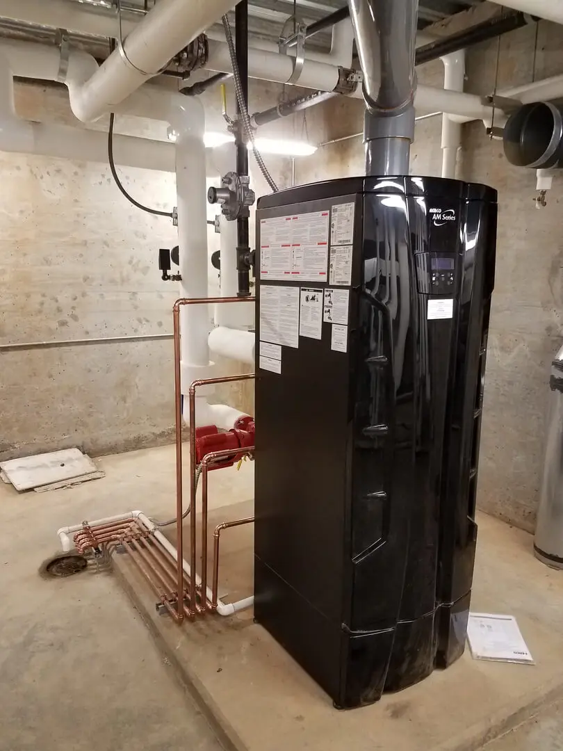 A black water heater in a basement with pipes.