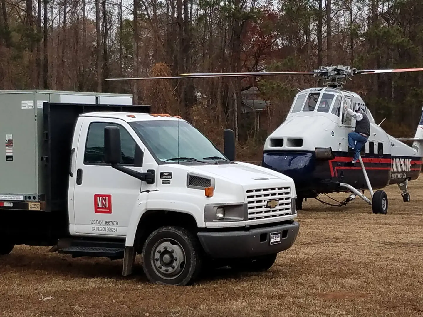 A truck parked in front of a helicopter with trees in the background